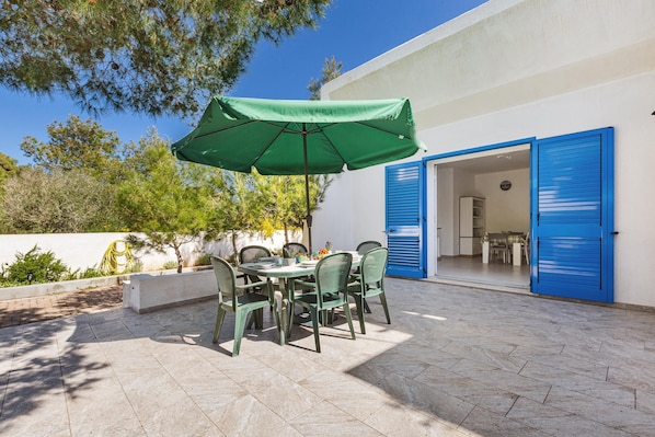 Un patio al aire libre con una mesa, sillas, una sombrilla verde y una puerta azul.