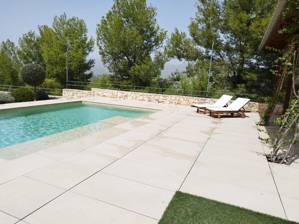 Una piscina con dos sillas de descanso y una pared de piedra.