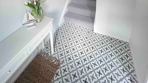 A staircase with patterned flooring, a white wall with a round mirror, and a hanging light fixture.