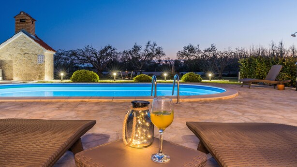 A swimming pool with a stone building in the background, a glass jar, and a glass of drink on a table. - Villa Paula (Privlaka)