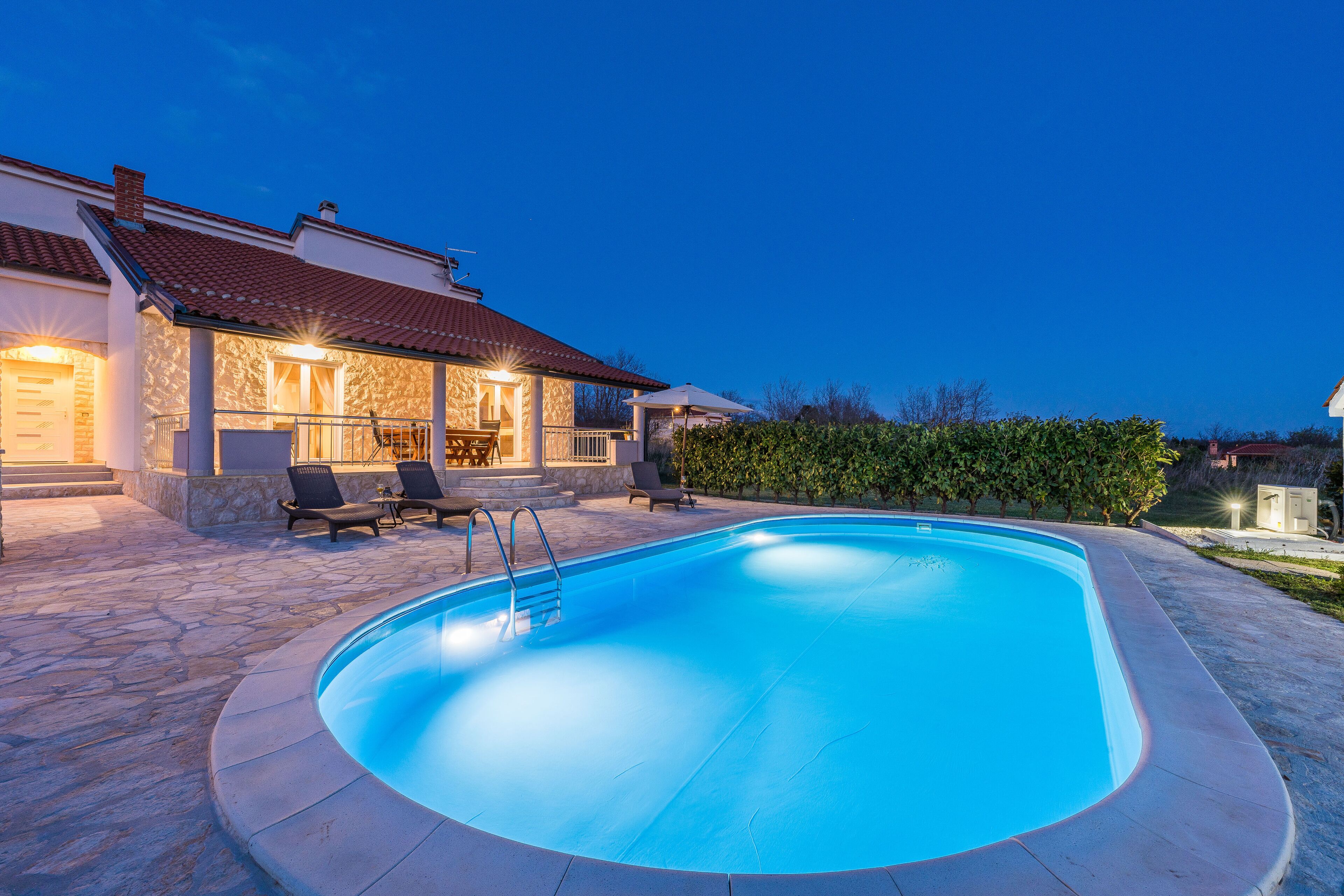A swimming pool with a stone deck, lounge chairs, and a covered patio area.