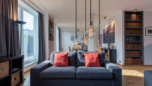 Un salón moderno con un sofá gris, cojines rojos, una estantería y lámparas colgantes.