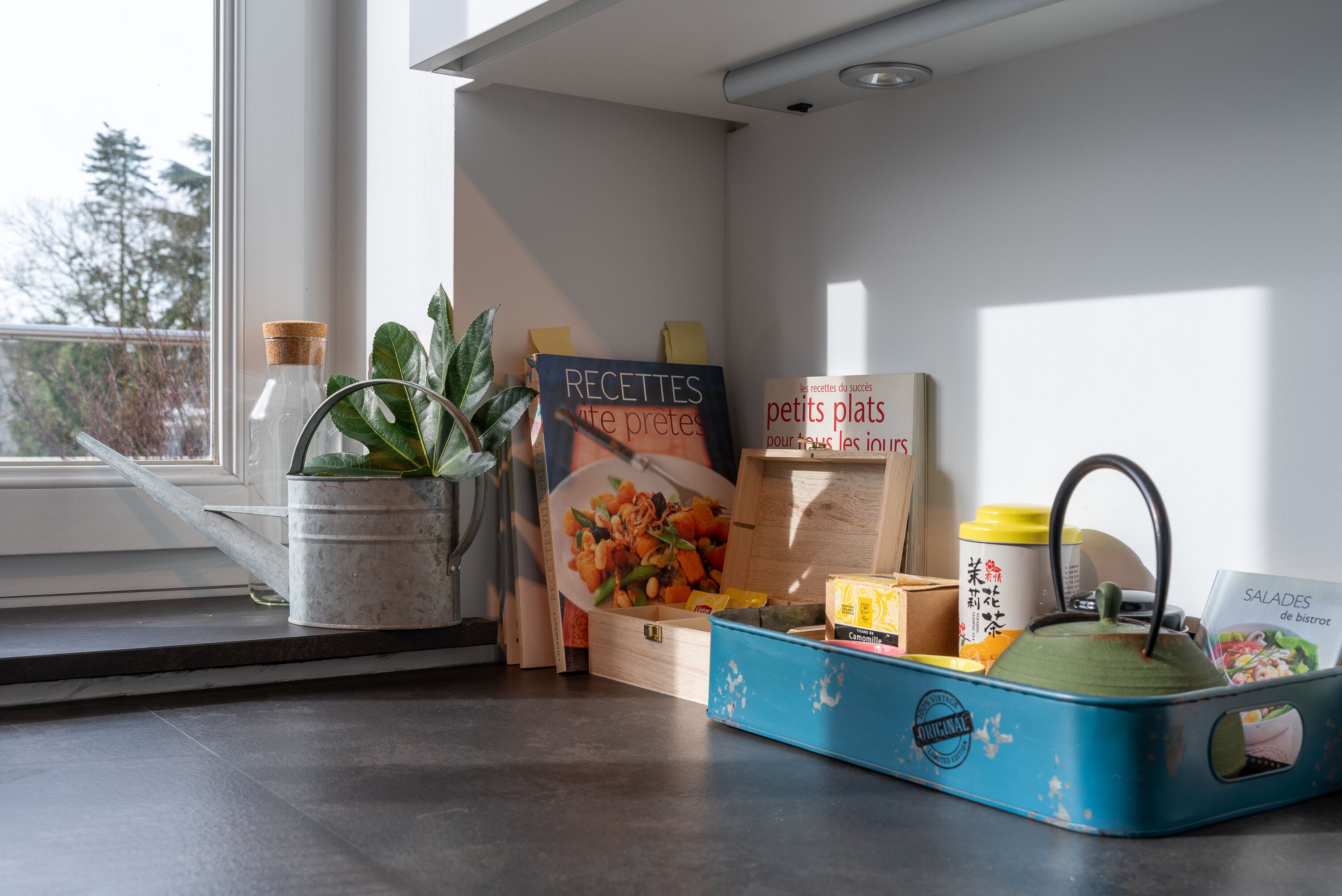 Una encimera de cocina con un libro de recetas, una tetera y un recipiente para alimentos.