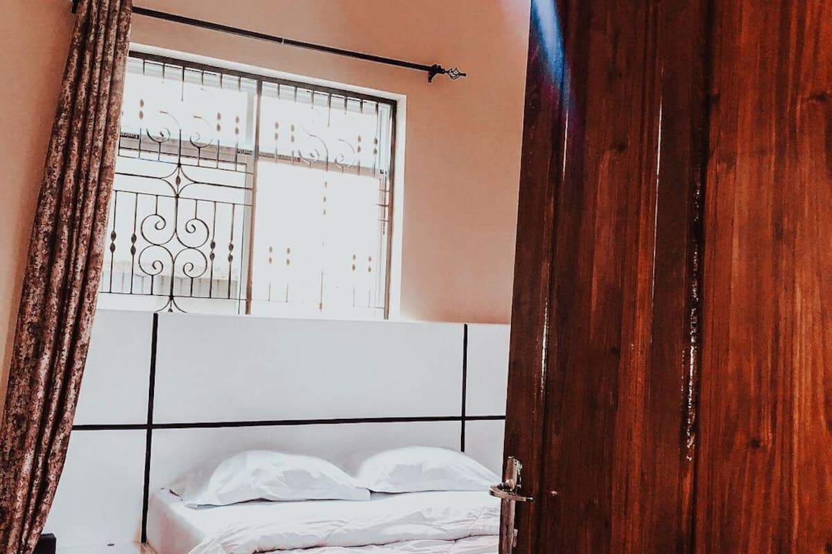 A bedroom with a wooden door, a bed with white bedding, a small bedside table, and a window with decorative iron bars.