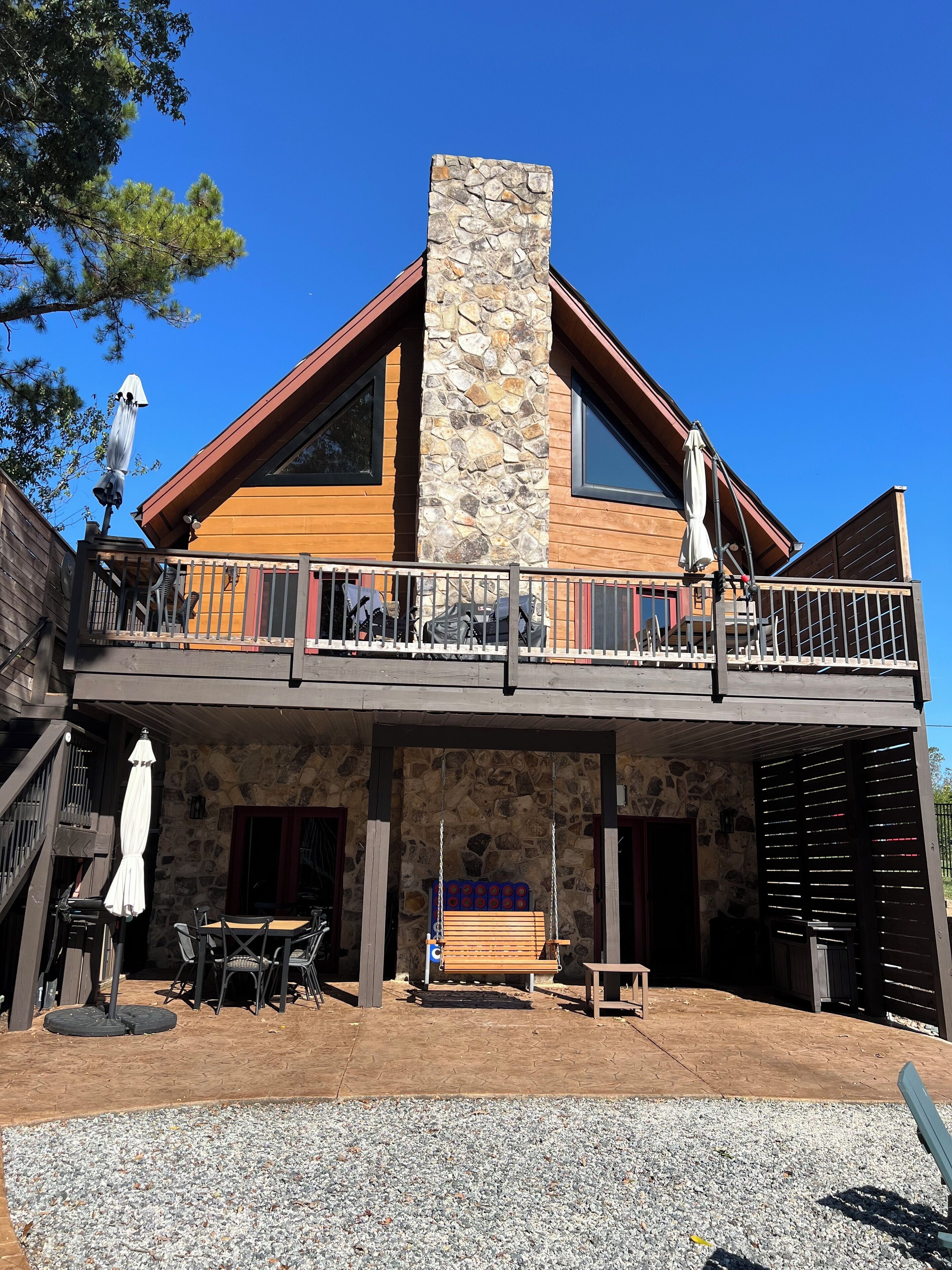 A two-story building with a stone chimney, wooden balcony, outdoor seating, and a stone facade.