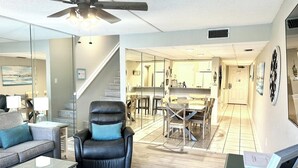 A spacious living room with a black leather chair, a grey sofa, and a dining area with wooden chairs.
