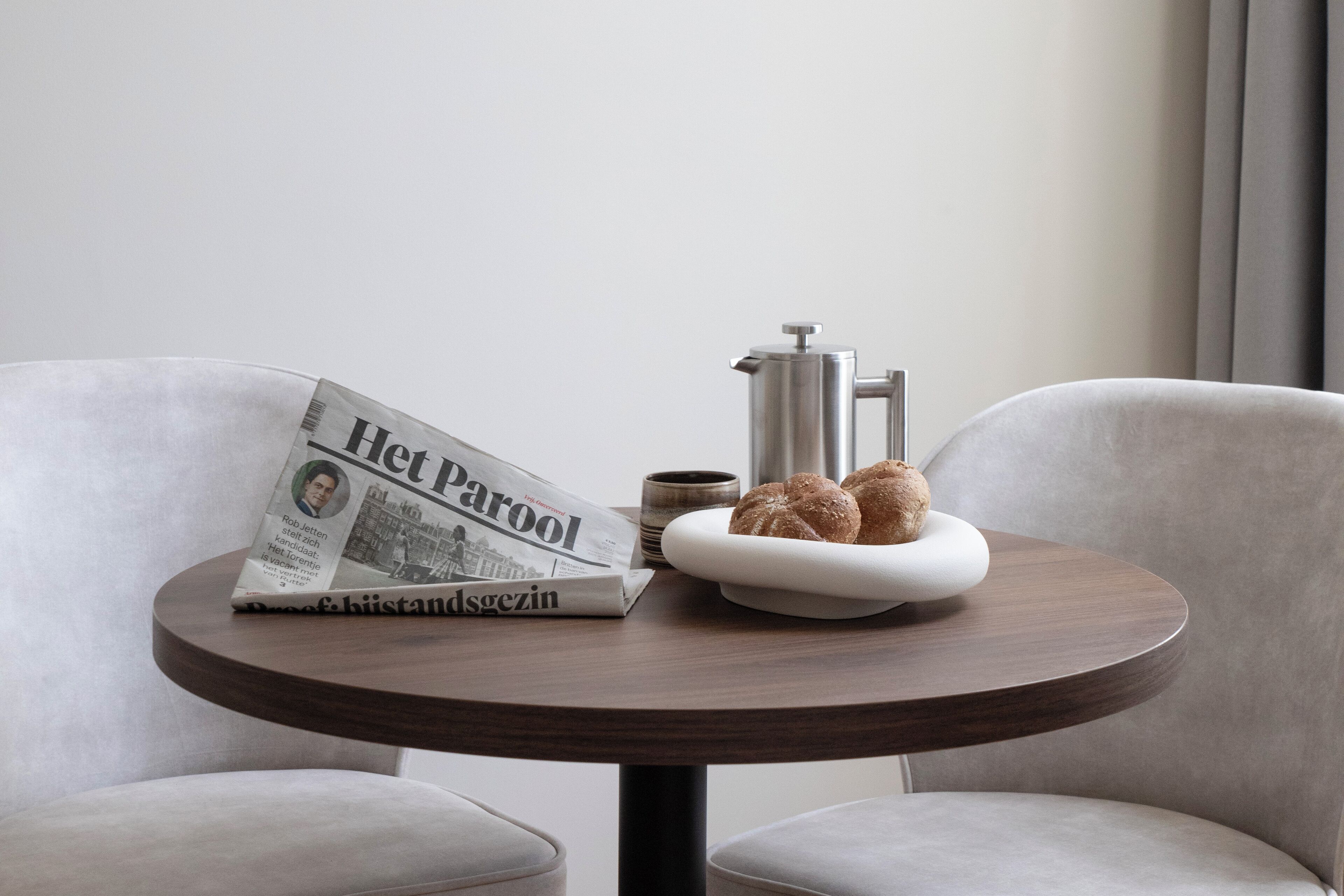 A round wooden table with a newspaper, a coffee cup, and a plate of pastries.