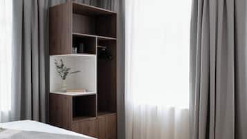 Une chambre à coucher avec un lit, une armoire en bois, une petite étagère avec une plante et des rideaux légers.