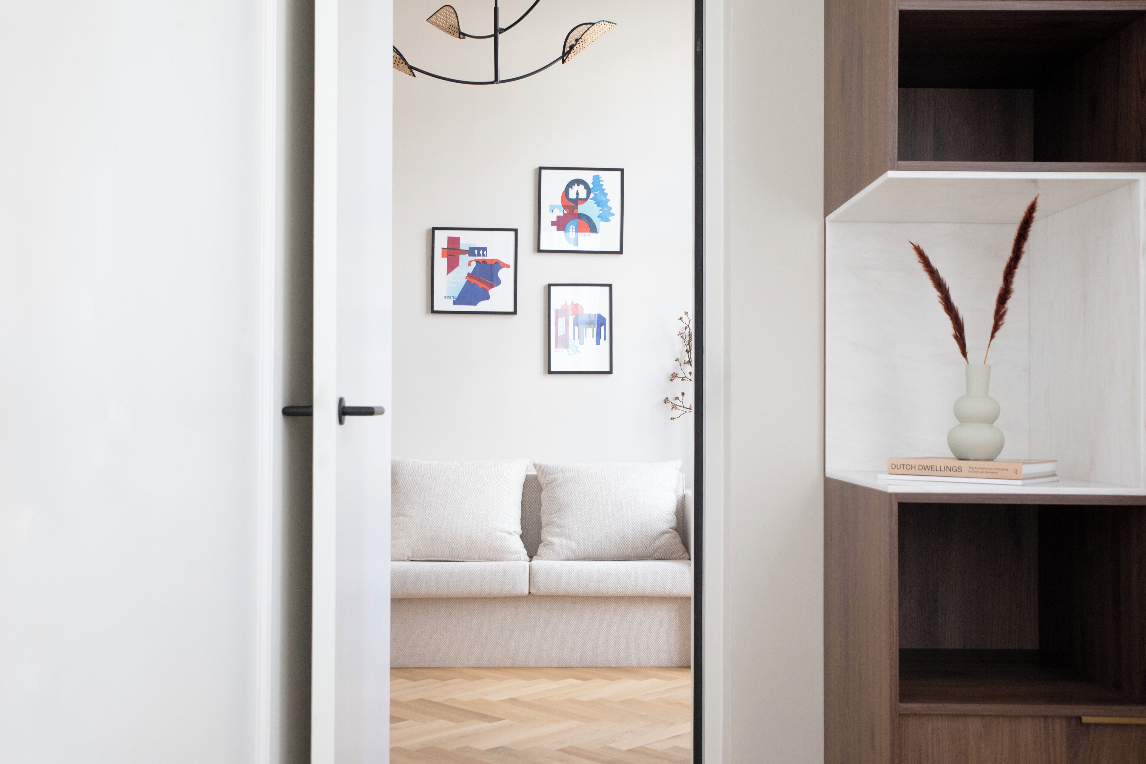 A modern interior with a white sofa, a wooden floor, and a shelf with decorative items.