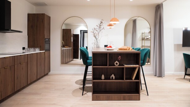 Una cocina moderna con armarios de madera, un comedor con sillas color turquesa y una estantería empotrada.