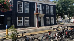 Un edificio histórico con una torre de reloj, una fila de bicicletas estacionadas adelante y un cielo azul despejado.