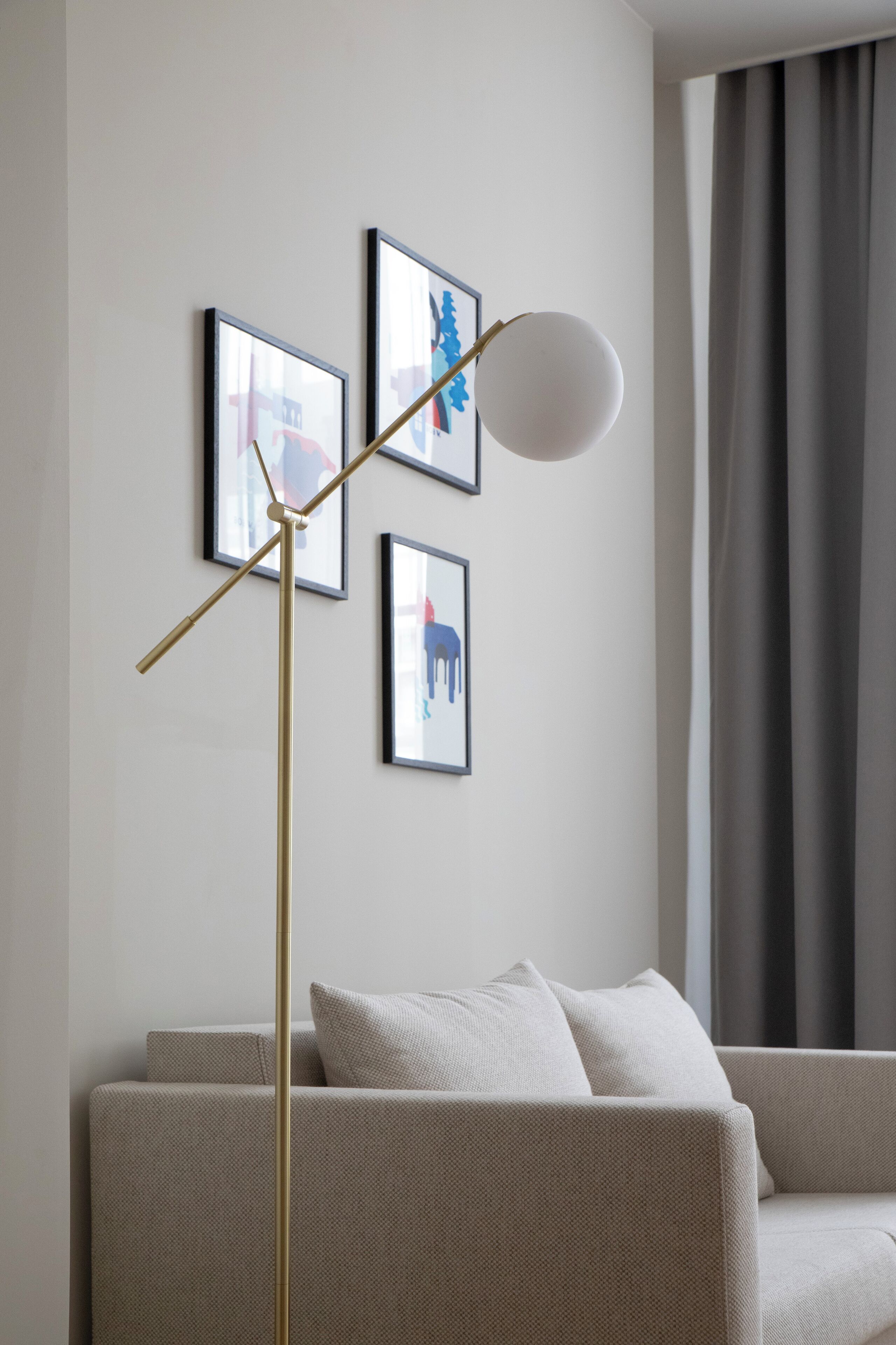 A modern living room with a sofa, a floor lamp, and three framed artworks on the wall.