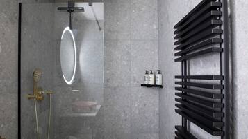 Un baño moderno con ducha de vidrio, toallero negro y un pequeño estante con artículos de aseo.