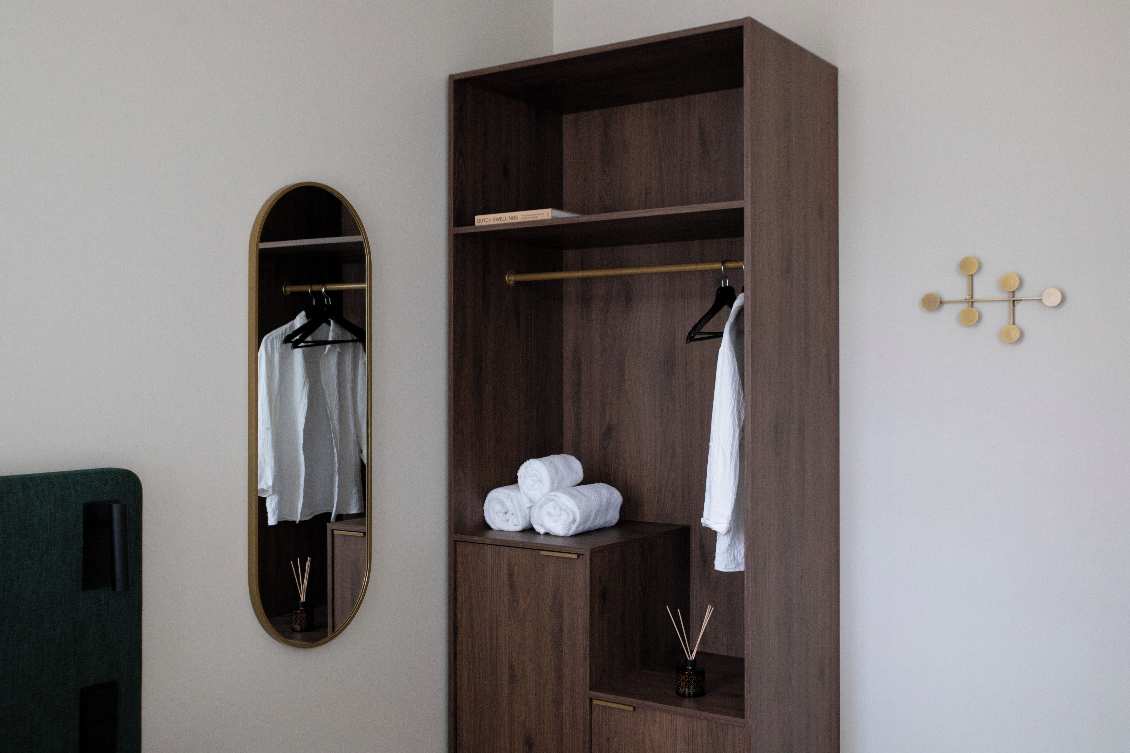 Een houten garderobe met spiegel, kledingroede en plank met opgerolde handdoeken.