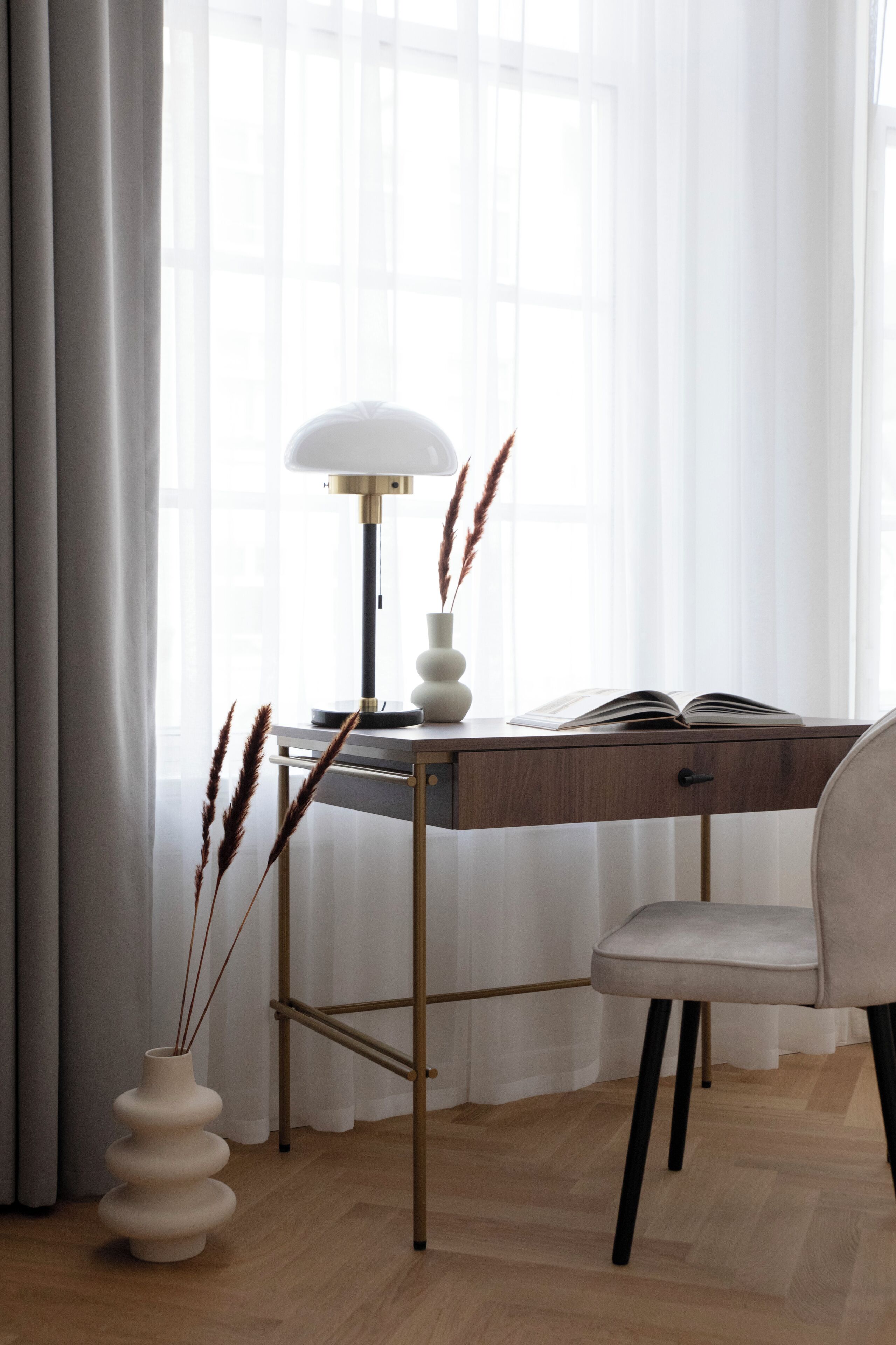 A modern desk with a lamp, a vase with dried plants, and an open book.