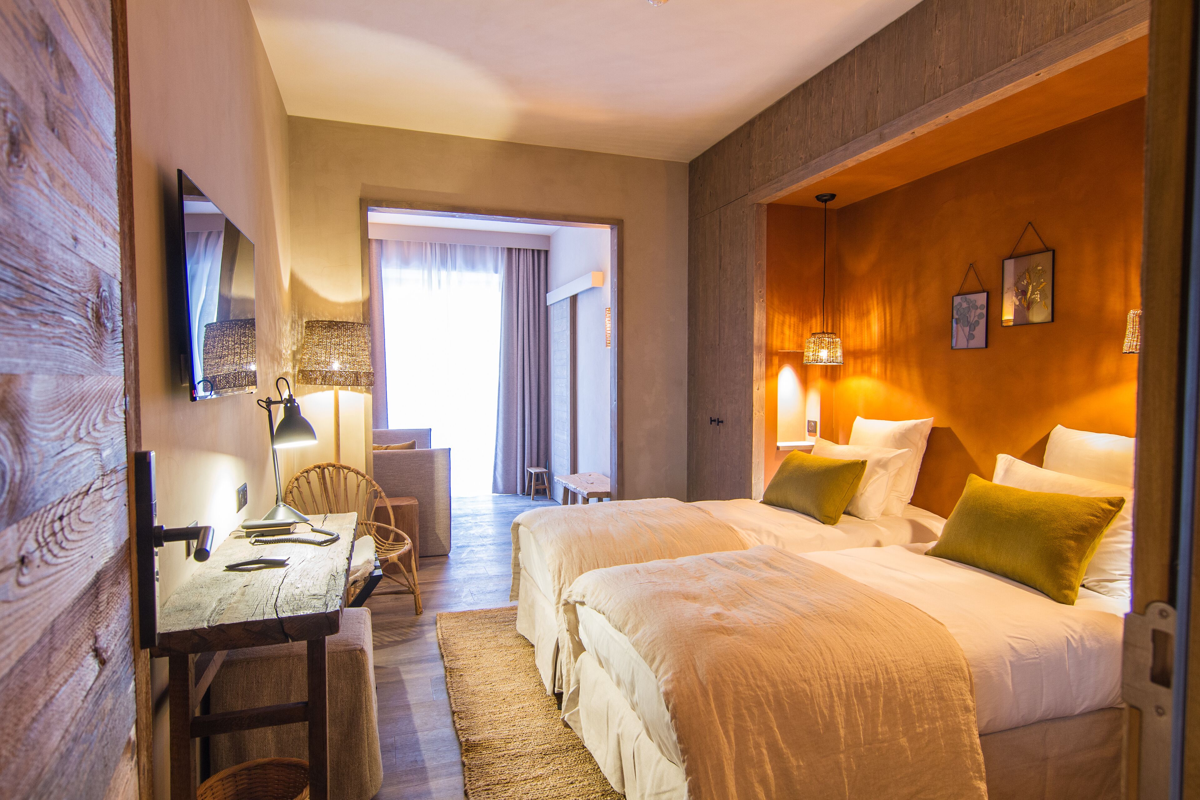A hotel room with a wooden desk, two beds, a chair, and a large mirror.