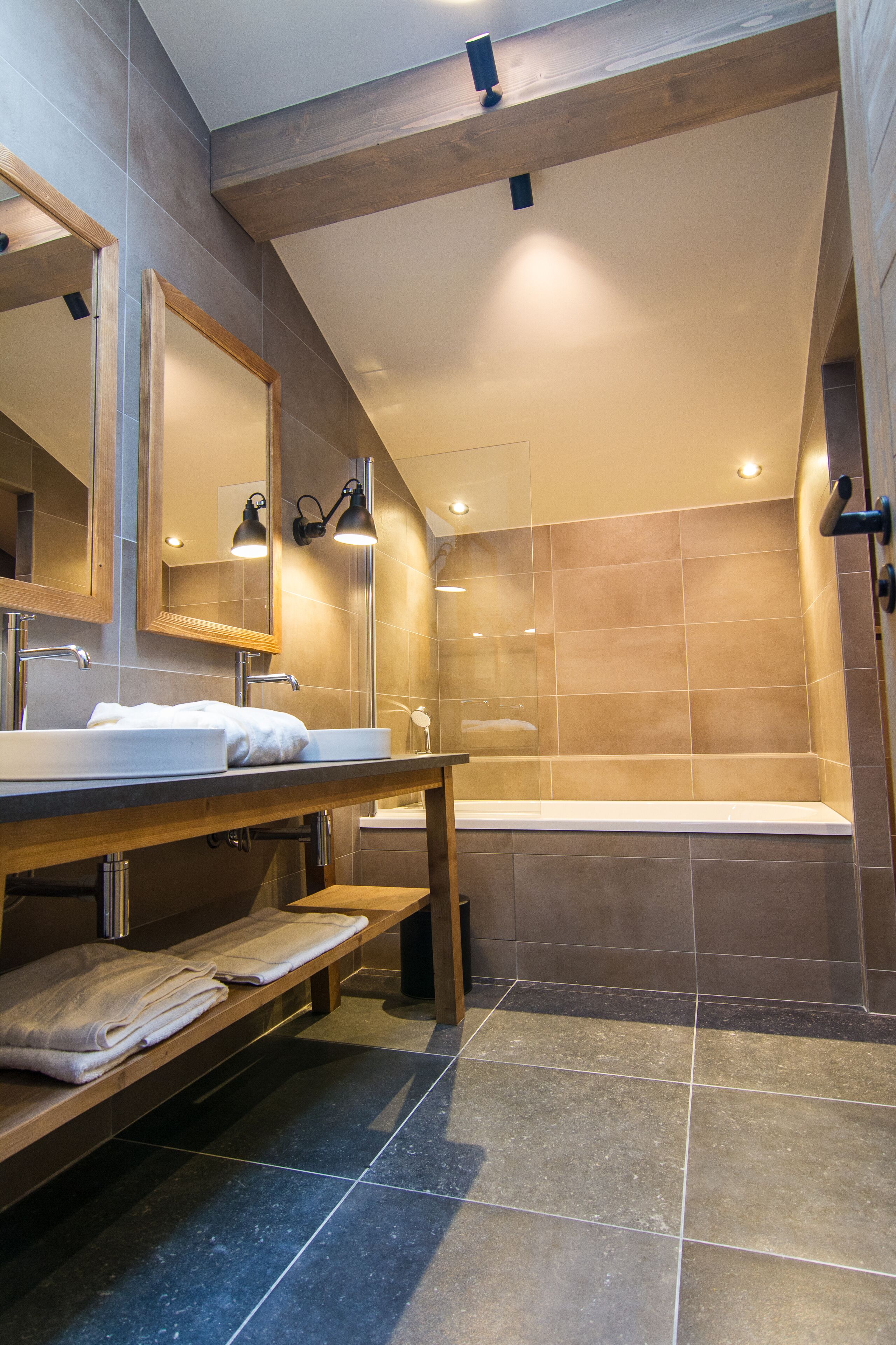 Ein modernes Badezimmer mit einem Holzkosmetikschrank, einem großen Spiegel, einer Badewanne und einer Sitzbank.