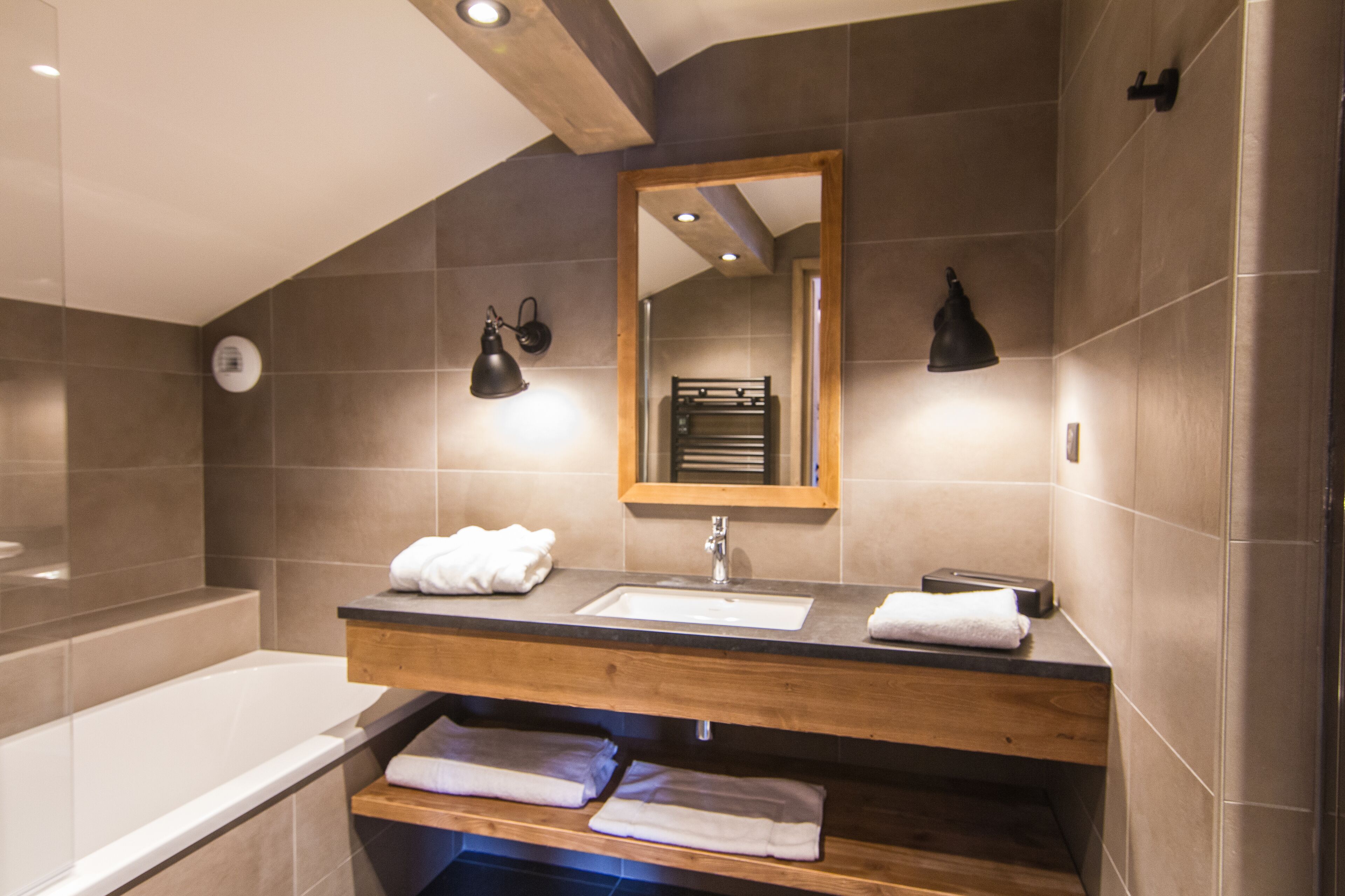 Een moderne badkamer met een houten wastafelmeubel, een grote spiegel en een bad.