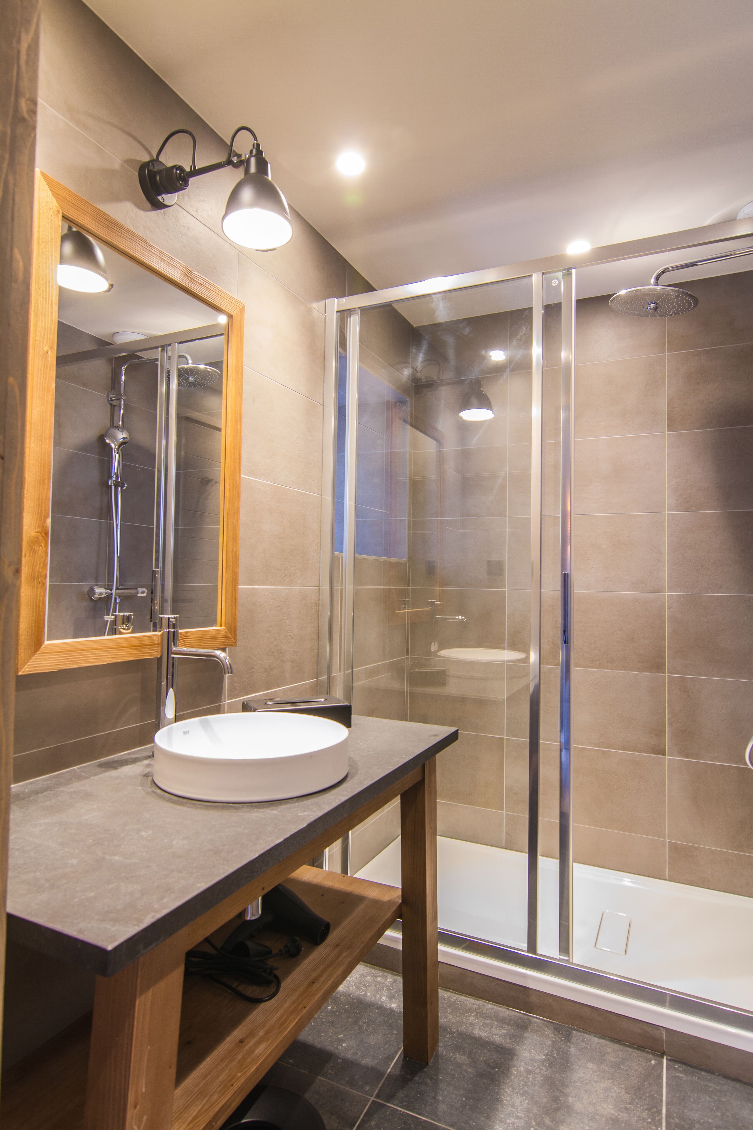 A modern bathroom with a wooden vanity, a glass shower enclosure, and a large mirror.