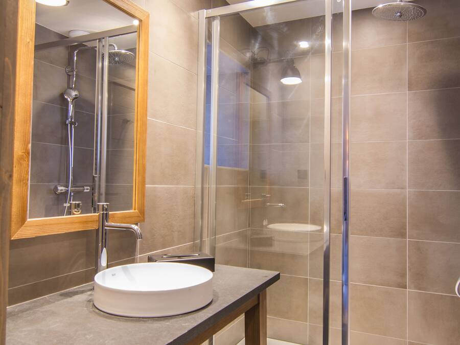 A modern bathroom with a wooden vanity, a glass shower enclosure, and a large mirror.