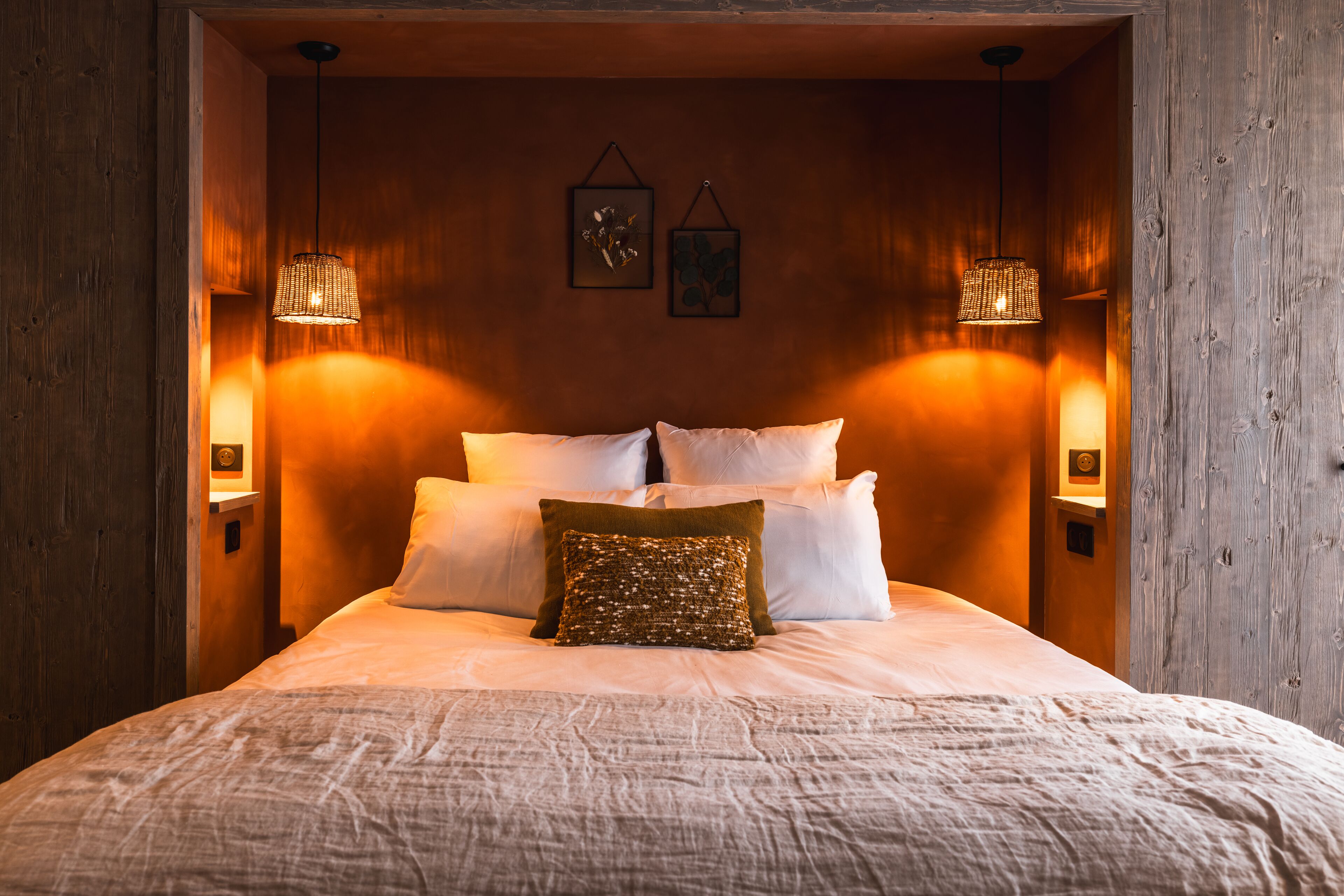 Una cama bien hecha con sábanas blancas y un cojín decorativo, flanqueada por dos lámparas de pared.