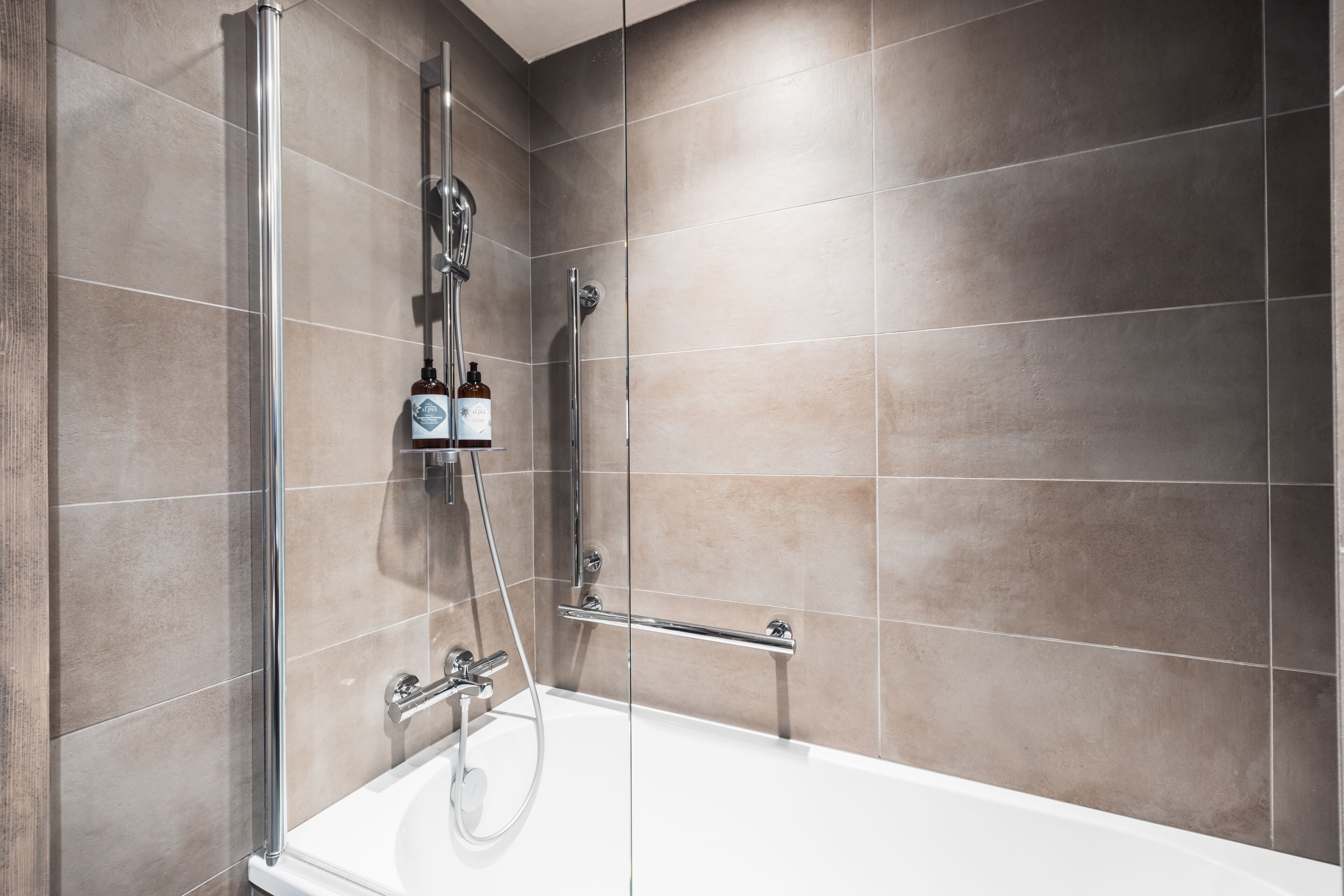 A modern bathroom with a glass-enclosed shower, a white bathtub, and beige tiles.