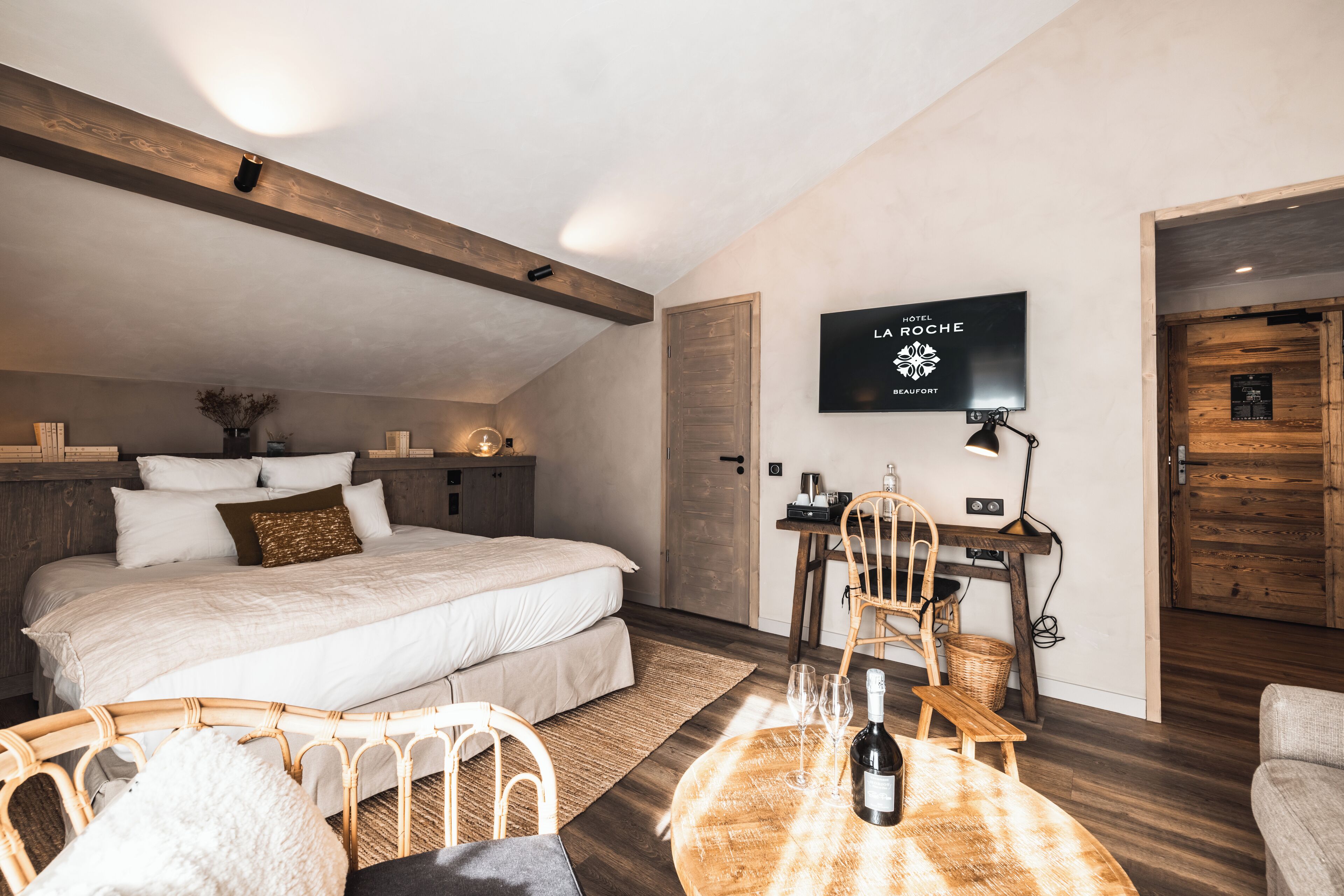 Een slaapkamer met een groot bed, een bureau met stoel, een televisie en een houten deur.