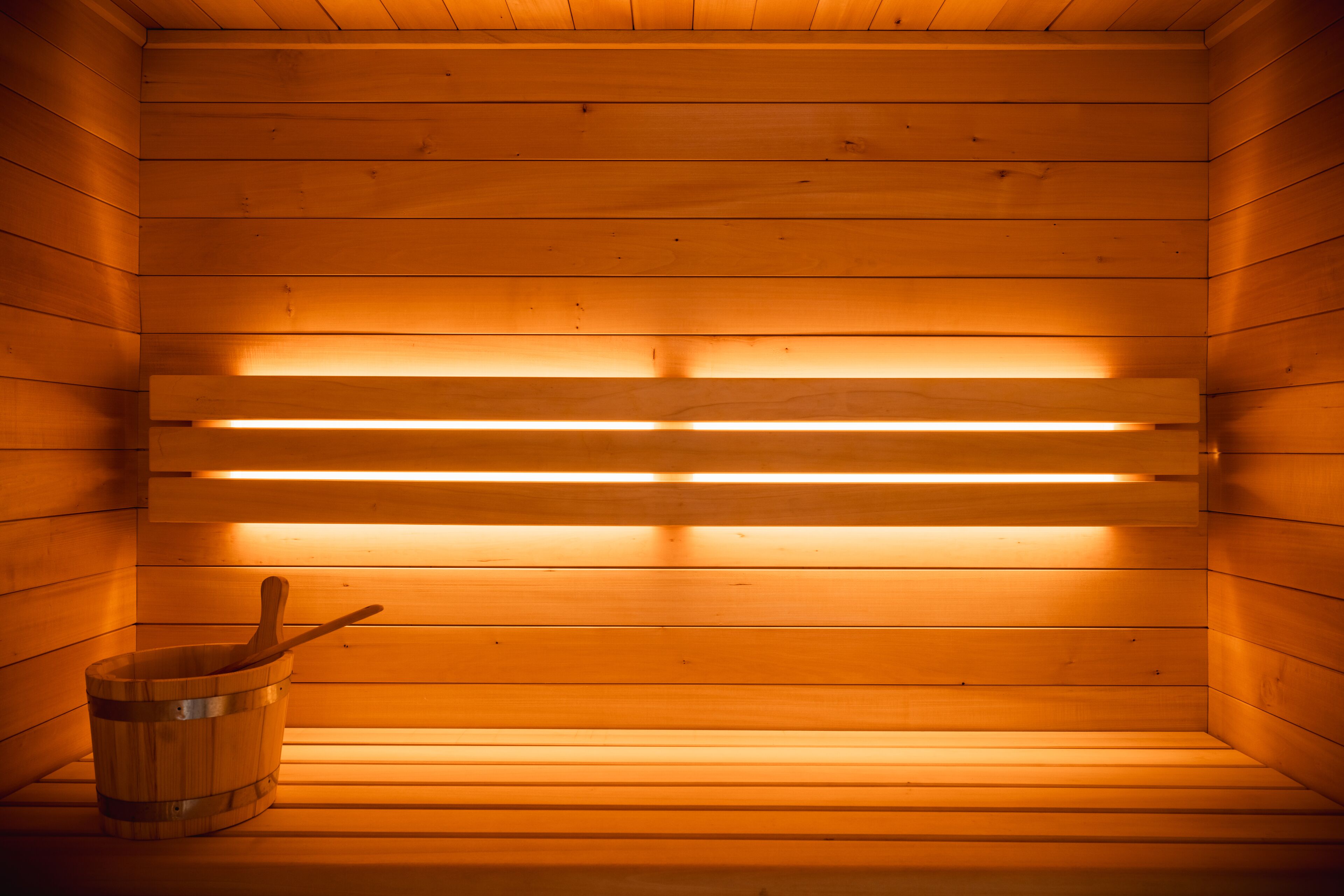A sauna with wooden walls and benches, a bucket with a wooden mallet, and a light fixture on the ceiling.