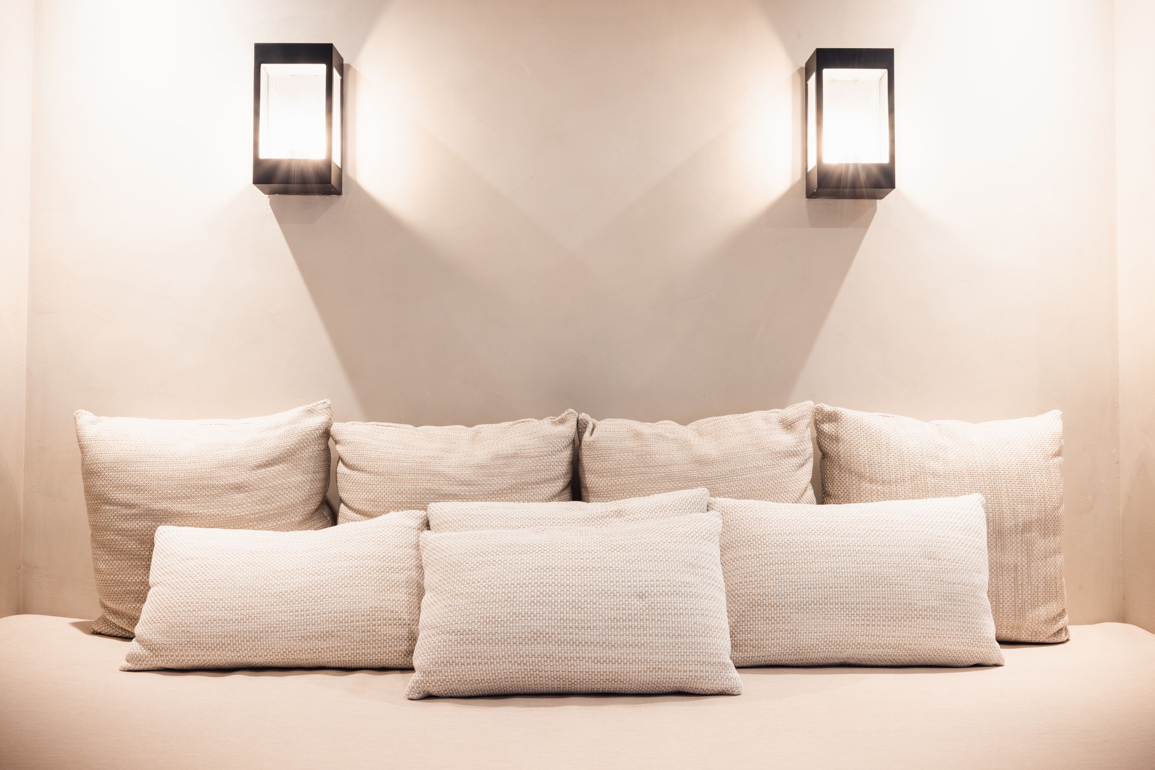 A bed with six pillows and two wall-mounted light fixtures.