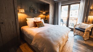 A bedroom with a large bed, wooden walls, and a balcony with a wicker chair. - Hotel de la Roche (Beaufort)