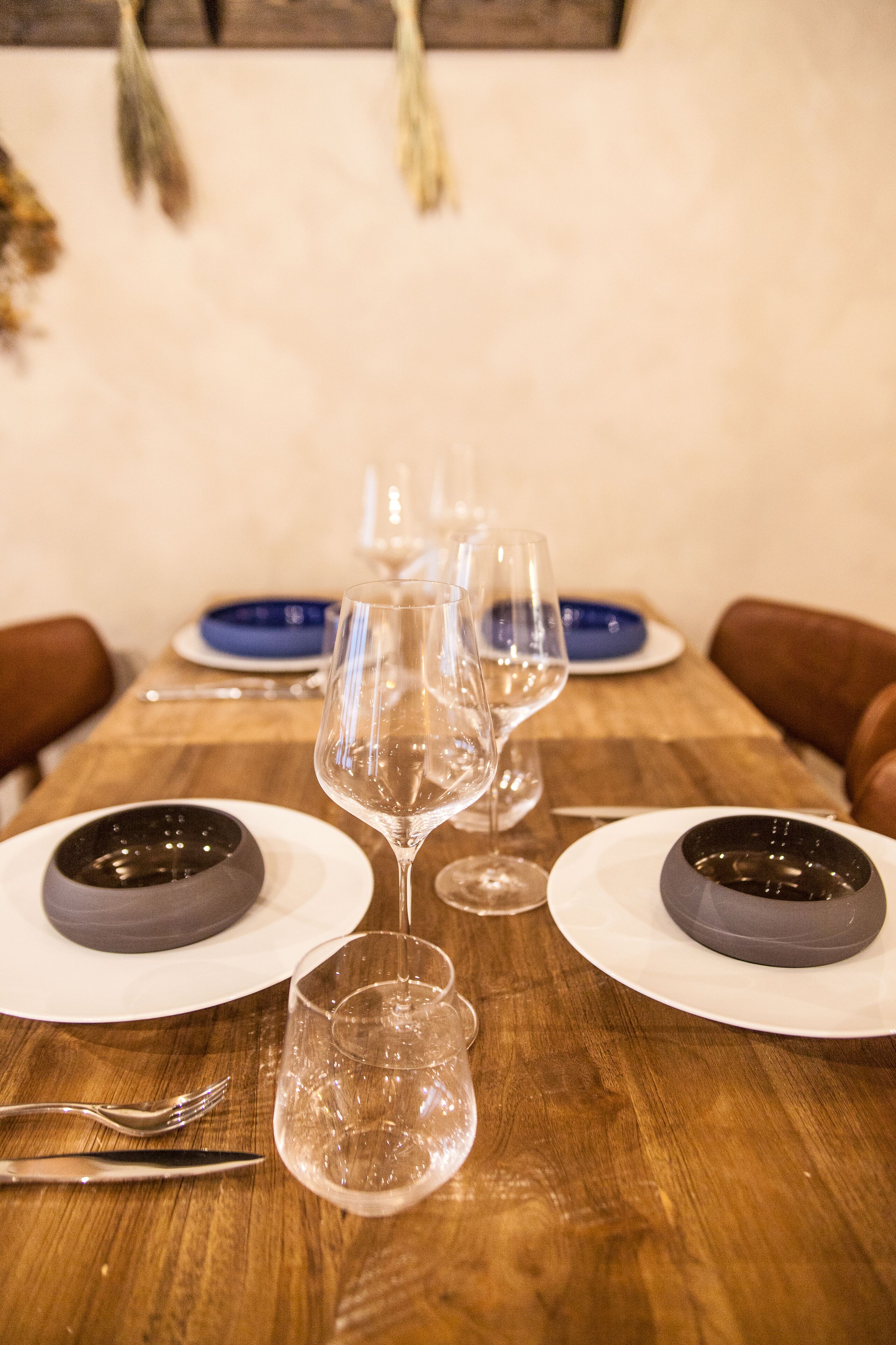 A dining table set with plates, bowls, and wine glasses, with chairs around it.