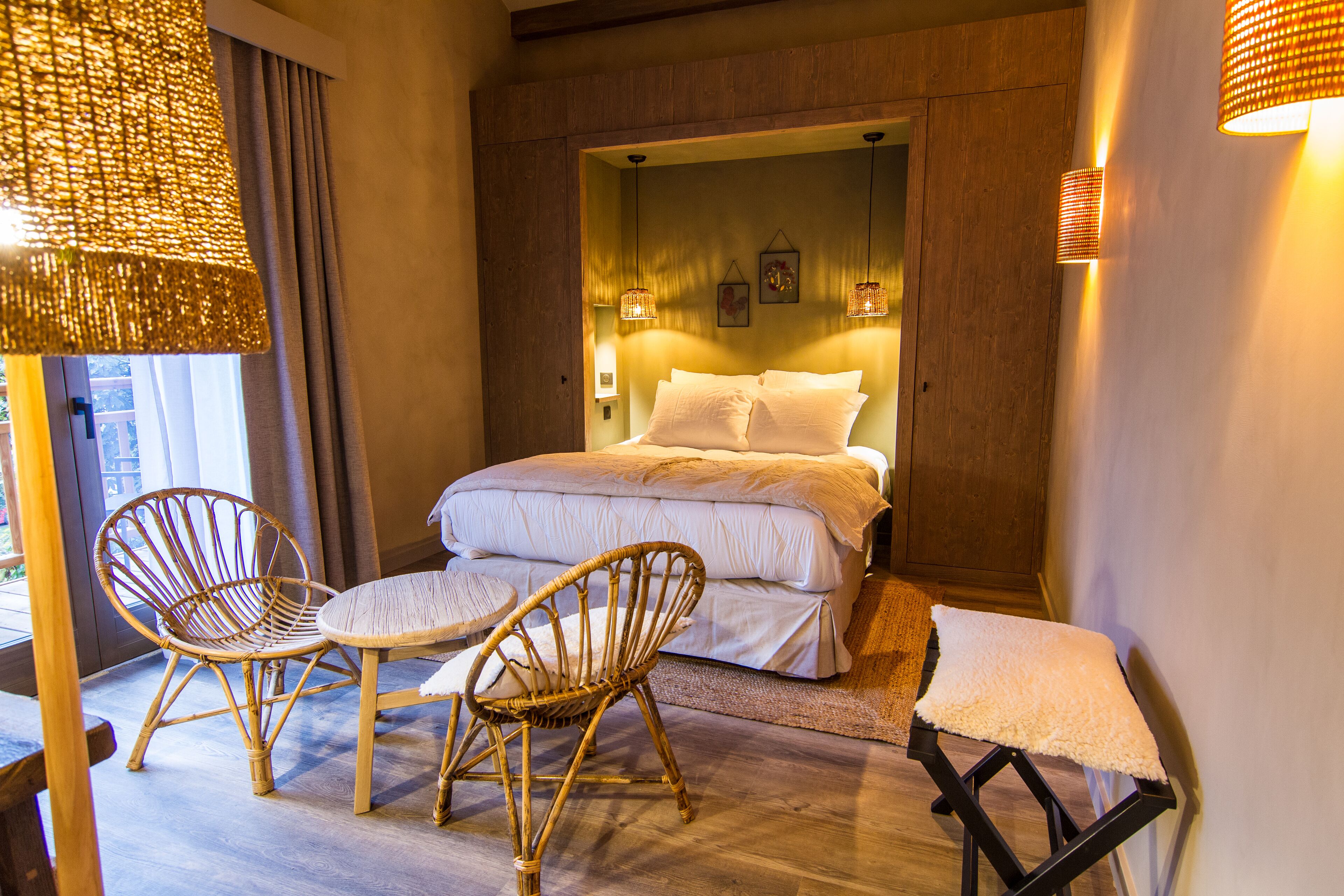 Un dormitorio con una cama, dos sillones de mimbre, una mesita y una mesilla de noche.