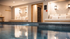 A modern indoor pool area with two seating areas, each with a sofa and a wall-mounted light fixture. - Hotel de la Roche (Beaufort)