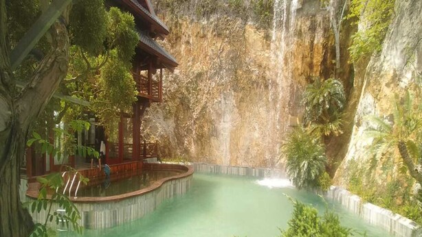 A serene indoor pool with a waterfall feature, surrounded by lush greenery and traditional wooden structures. - Minawa Kenhga Resort & Spa Ninh Binh (Gia Vien)