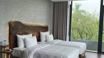 Una habitación de hotel moderna con dos camas, un ventanal con vistas a zonas verdes, un cabecero de madera y una pequeña mesa redonda.