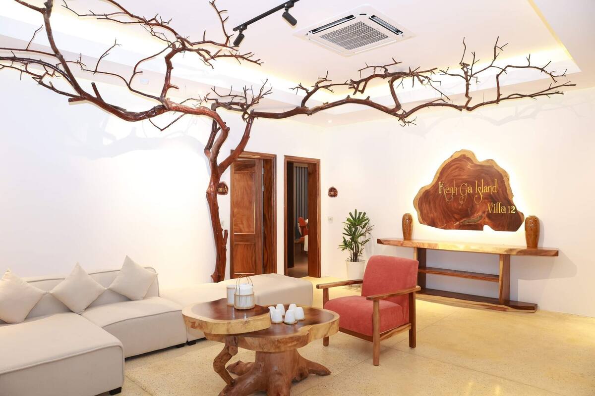 Ein modernes Wohnzimmer mit einer Astinstallation, einer Couch, einem roten Sessel, einem Holztisch und einem Schild mit der Aufschrift 'Kenh Gia Island Villa 12'.