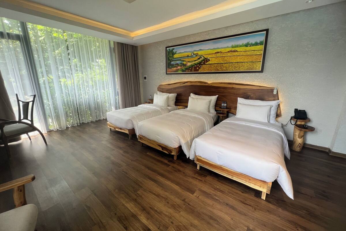 Ein Hotelzimmer mit drei Betten, einem Essbereich und einem großen Fenster mit Vorhängen.