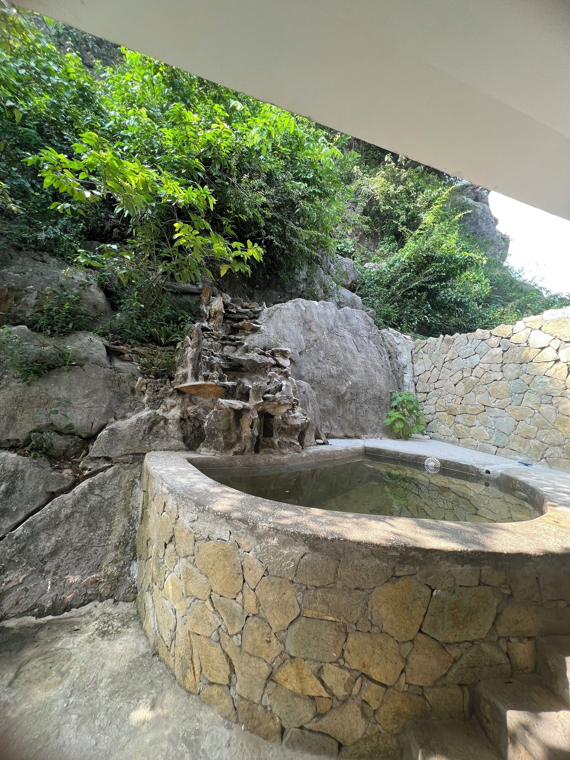 A stone fountain surrounded by lush greenery and a rocky landscape.