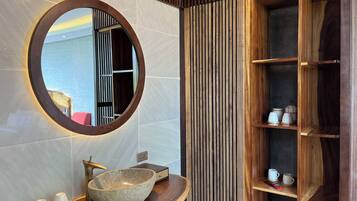 A bathroom with a round mirror, a stone sink, and wooden shelves.
