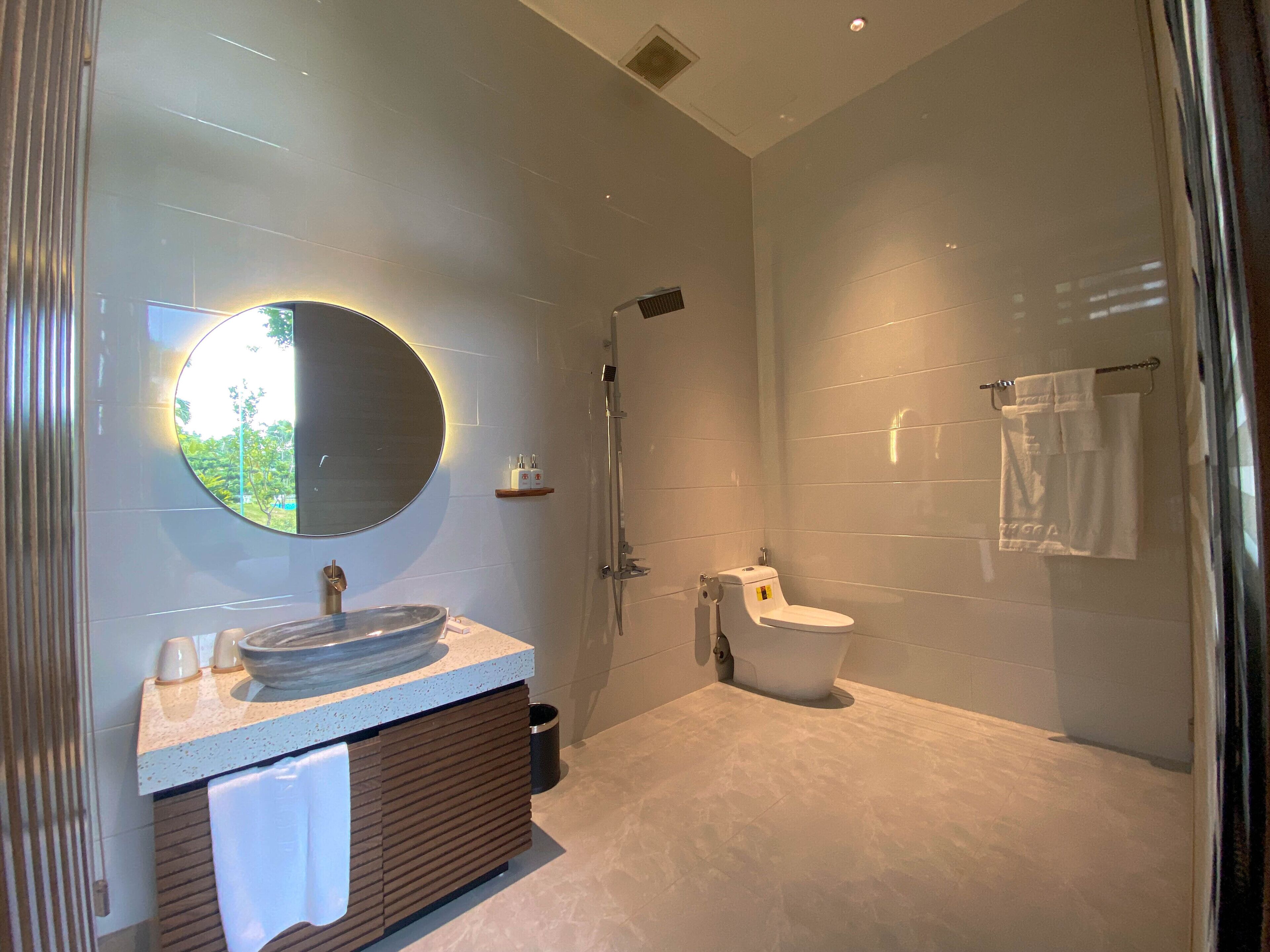 Un baño moderno con un espejo redondo, un lavamanos y un inodoro.