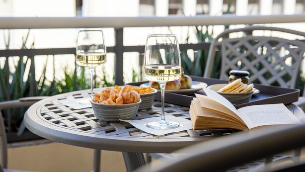 A round metal table with a book, two wine glasses, a bowl of bread, and a tray with bread. - La Musa Apartments & Rooms (Palermo)