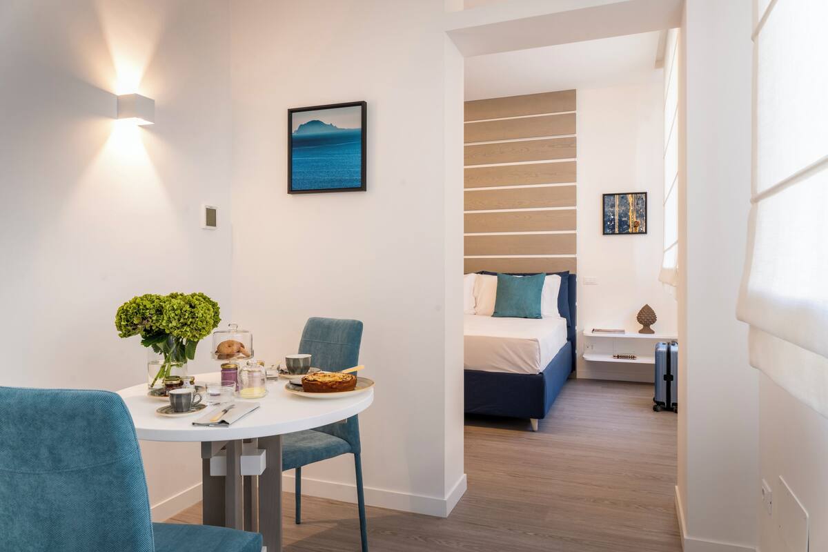 A modern hotel room with a dining area, a bed with a view, and a small side table.