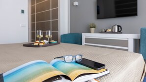 A hotel room with a bed, a book, glasses, a smartphone, a tray with glasses and pastries, a coffee maker, and a TV on the wall. - La Musa Apartments & Rooms (Palermo)