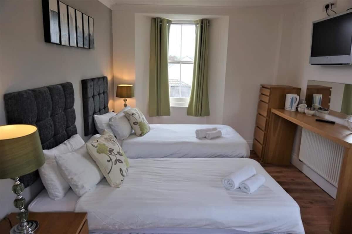 A hotel room with two beds, a desk, a TV, and a window with curtains.
