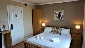 A neatly arranged bedroom with a bed, bedside lamps, a wooden wardrobe, and a wall-mounted artwork.
