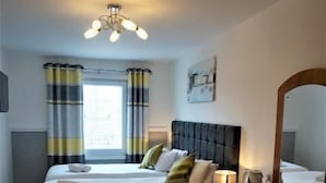 A hotel room with two beds, a large mirror, a wooden dresser, and a ceiling light fixture. - Rooms at The Angel (Cardigan)