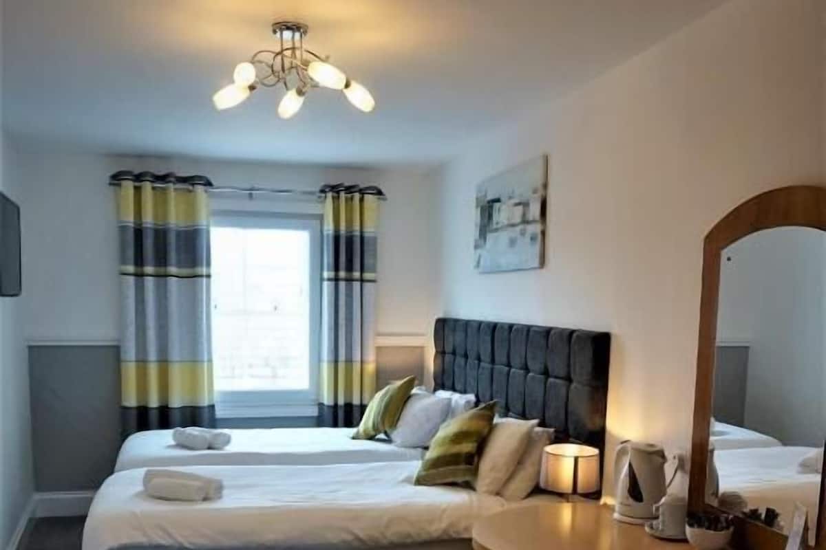 A hotel room with two beds, a large mirror, a wooden dresser, and a ceiling light fixture.
