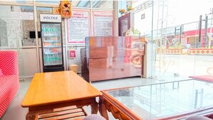 A hotel lobby with a red patterned sofa, a wooden table, a minibar, and a glass railing. - Sanjog Resort (Kota)