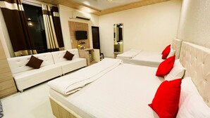 A hotel room with a sofa, two beds, a TV, a mirror, and a window with curtains. - Sanjog Resort (Kota)