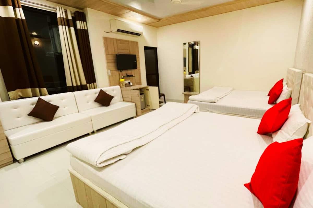 A hotel room with a sofa, two beds, a TV, a mirror, and a window with curtains.